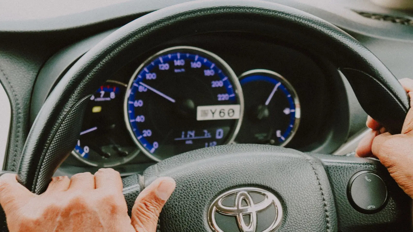 Manos de una persona mayor sobre el volante de un auto con el tablero encendido