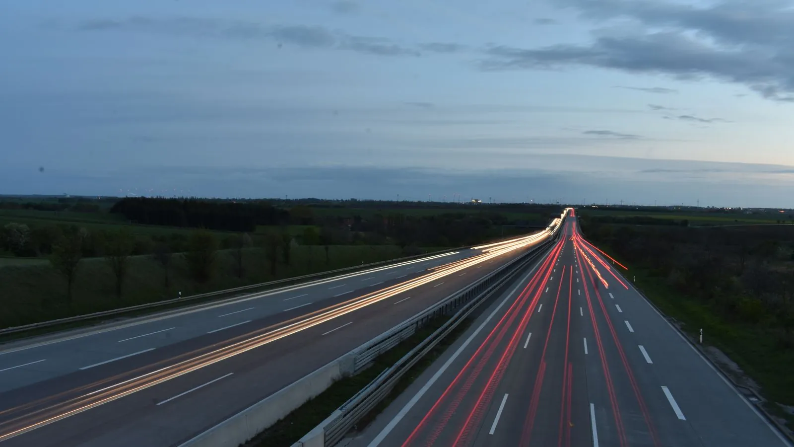 Autopista interurbana al atardecer con estelas de luz de vehículos en ambas calzadas