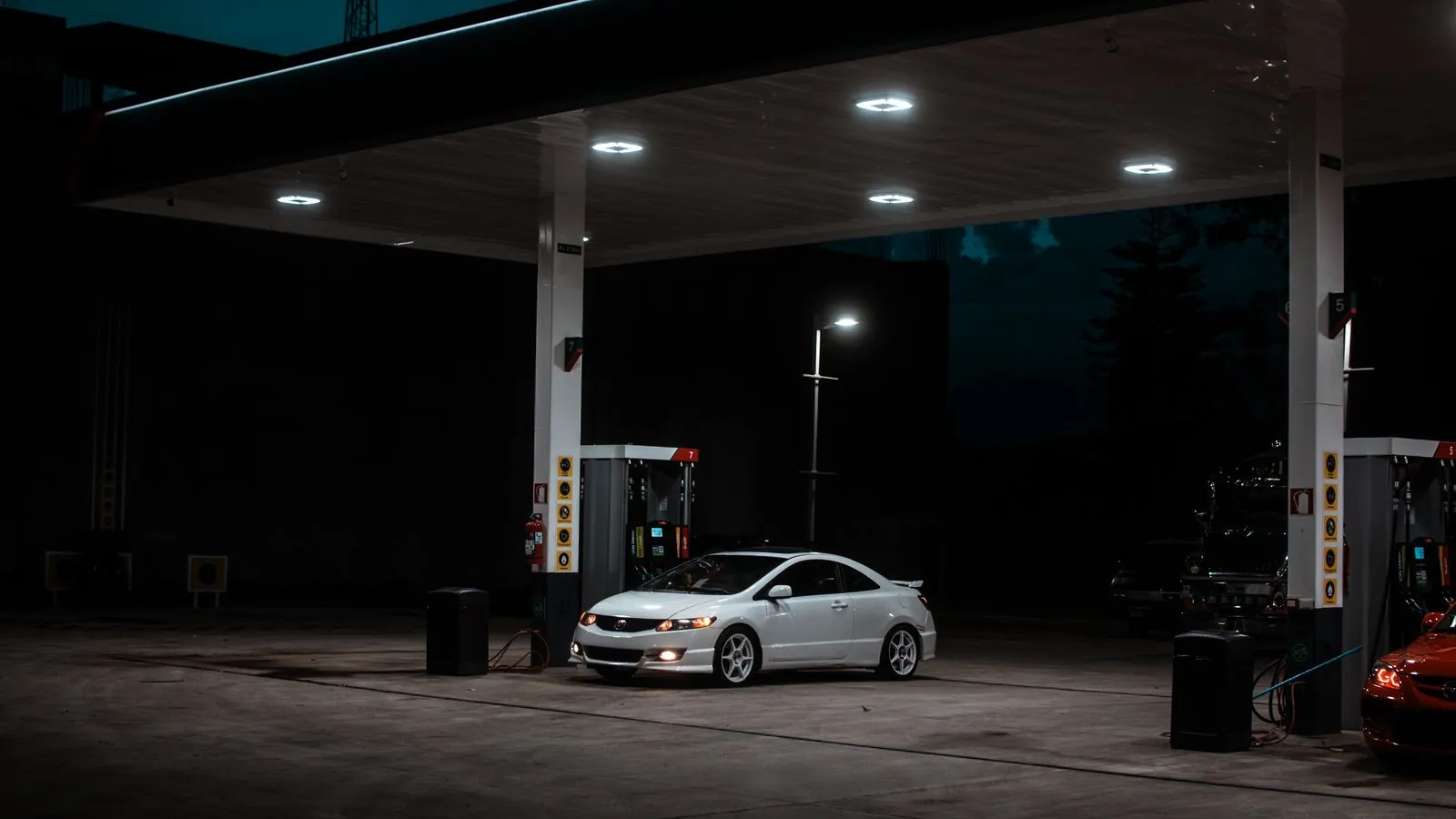 Auto solitario detenido de noche bajo la techumbre iluminada de un servicentro